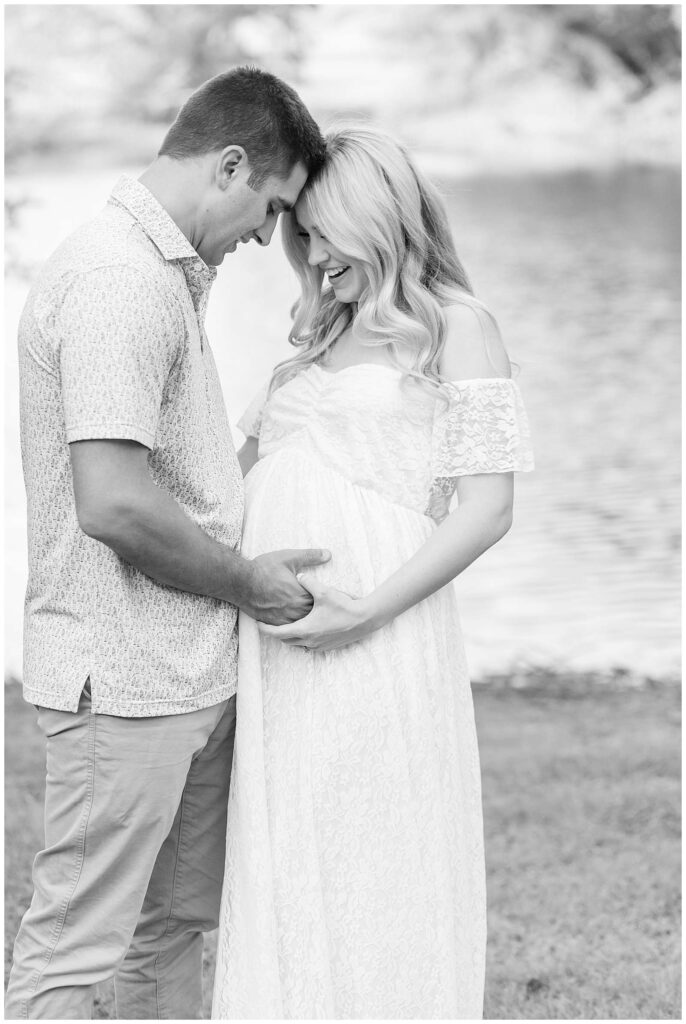 McKinney maternity photographer, Wisp + Willow Photography, take a beautiful black and white image of the expecting parents with their foreheads touching and holding hands together on her baby belly.