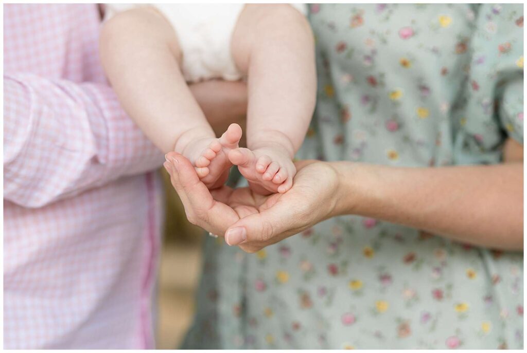 Up-close detail shot of baby toes being held in the palm of her mother's hand. 