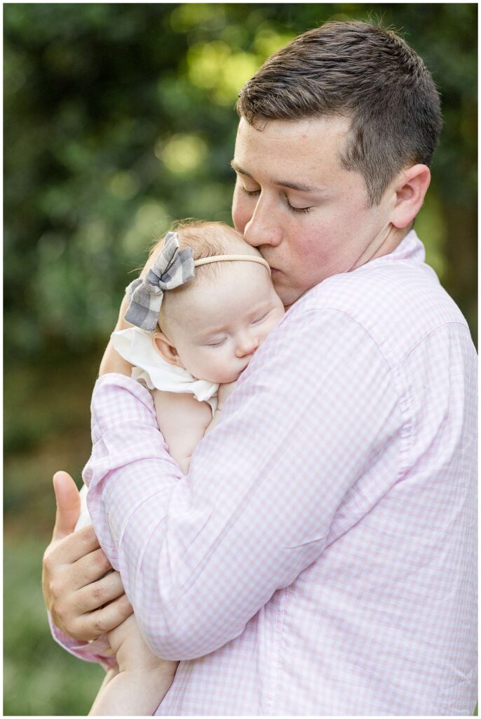 New young dad holds his newborn baby girl asleep on his shoulder as he gives her a kiss on her head.  See more on the Wisp + Willow Photography Co. blog to see more of this sweet session.