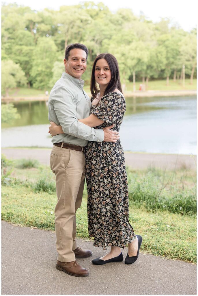 Couple stands belly to belly, coordinating with a pop of blue, khaki, and a black floral dress as they smile at the camera of Wisp + Willow Photography Co.