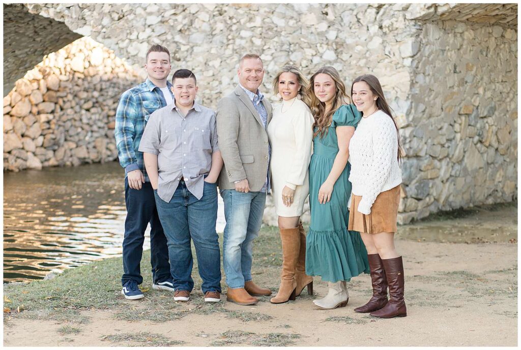 Family of 6, 2 teenage daughters and 2 teenage sons, stand under the bridge at Adriatica Village for their fall family portrait session with Wisp + Willow Photography Co.  
