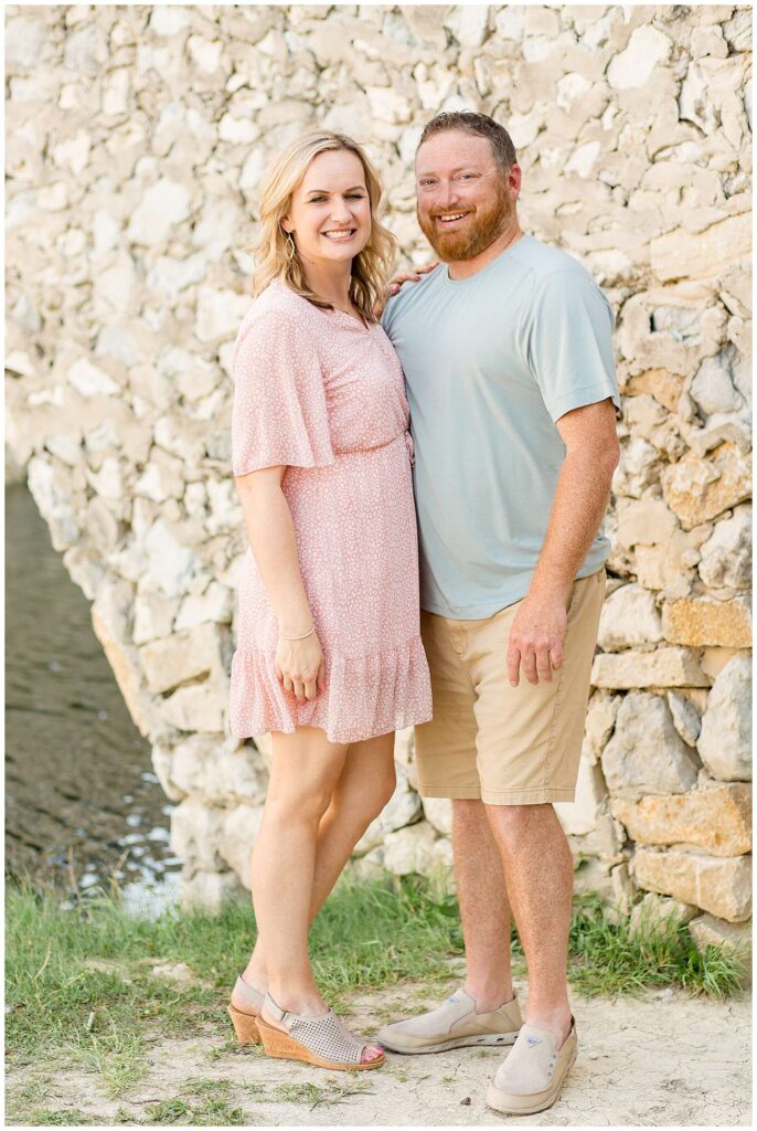 Mom and Dad stand together, mom wearing a pink and white dress and Dad wears a mint tshirt and khaki shorts as they smile together during their family session.