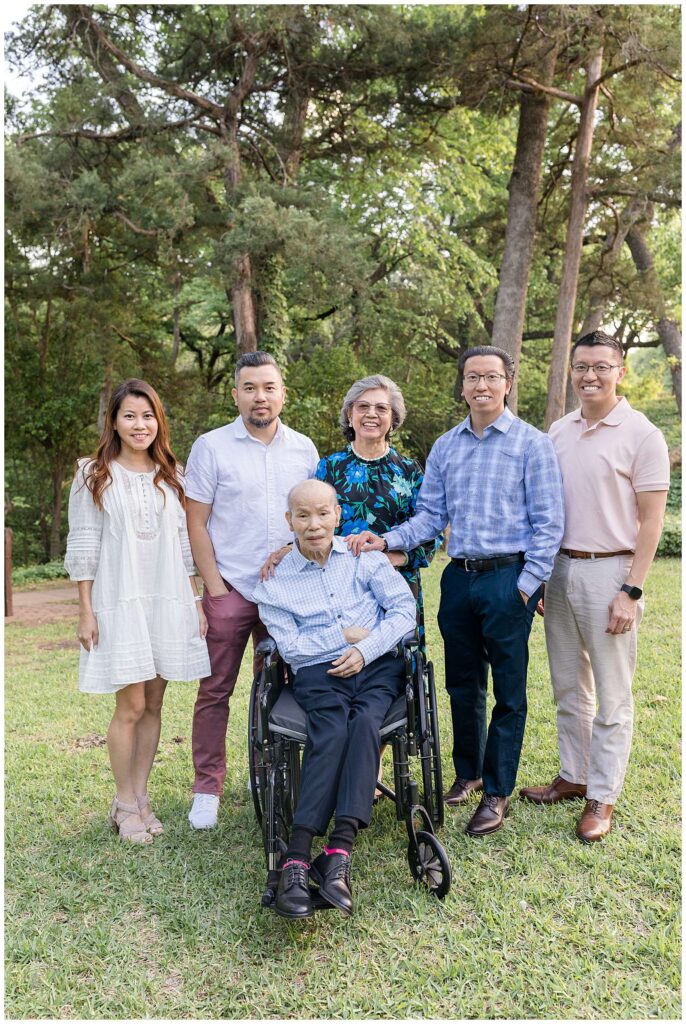 Extended family portraits with Wisp + Willow Photography Co. in Dallas, TX shows Grandpa in a wheelchair, Grandma standing behind him and them surrounded with their 3 sons and 1 daughter.