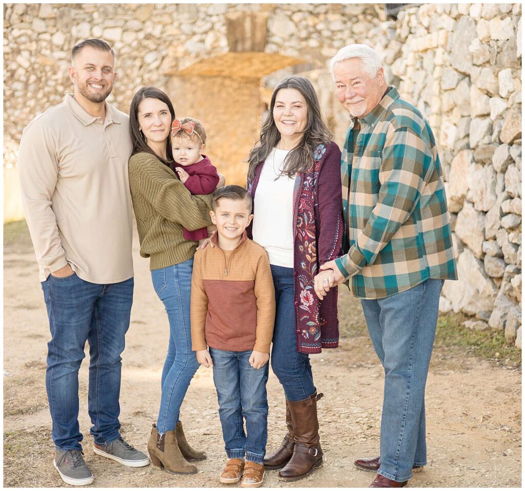 Extended family portraits at Adriatica Village consist of Grandma and Grandma with their daughter and her husband and two kids- 1 daughter and 1 son.  They stand in a line and smile at the camera of Wisp + Willow Photography Co.