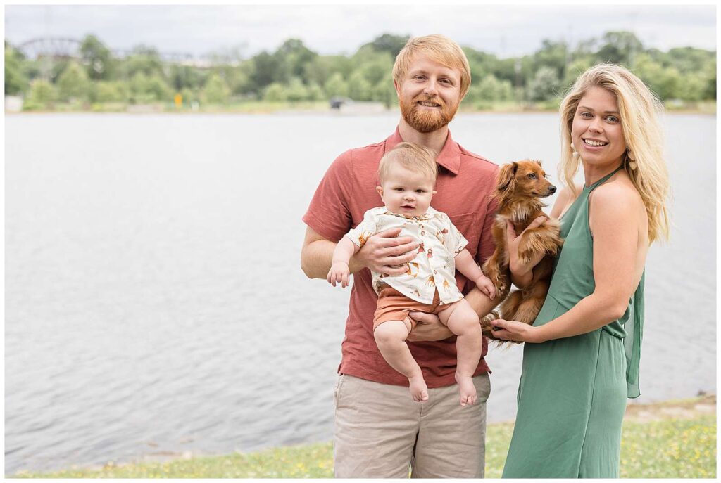 Parents with their new 6 month old son and Dachsund dog take family portraits in Nashville, TN.  Mom wears a green dress and a the boys coordinate in a rust orange colors.