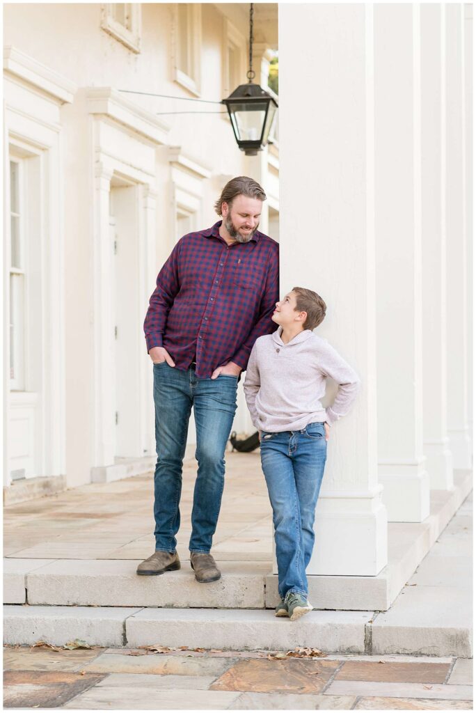 Father and son stand against a white pillar with their hands in their jeans and look at each other smiling on the visitor steps of Chickamauga Battlefield during their Chattanooga family session.