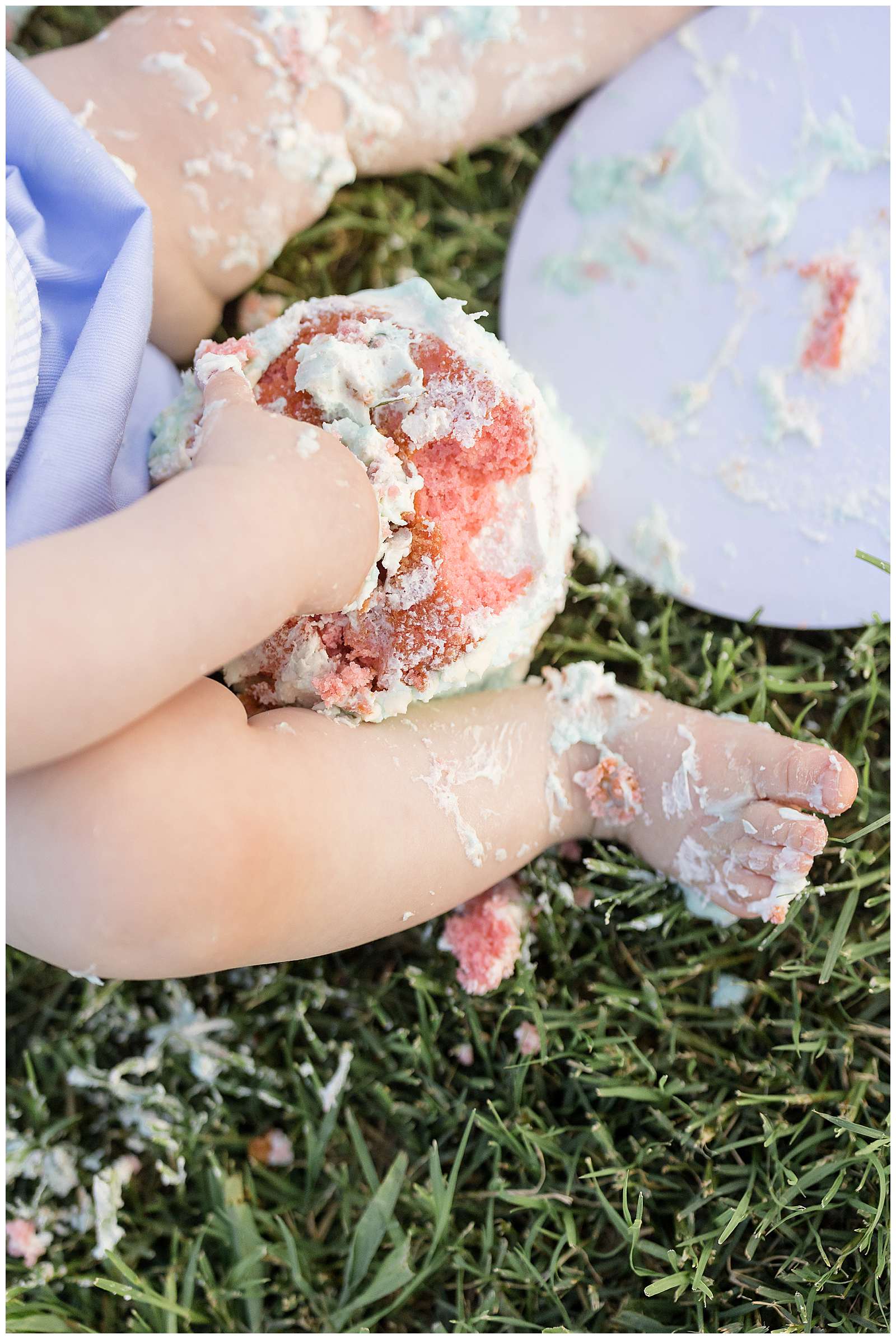 Detail image of baby's hand in their strawberry cake with vanilla icing smash cake and one foot of baby toes covered in icing.