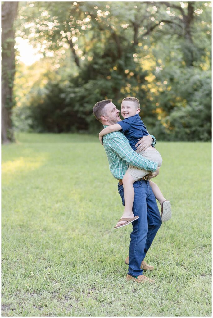 Dad picks up his elementary aged son as he looks at him and makes his son laugh during their family portraits at Erwin Park in McKinney, TX!