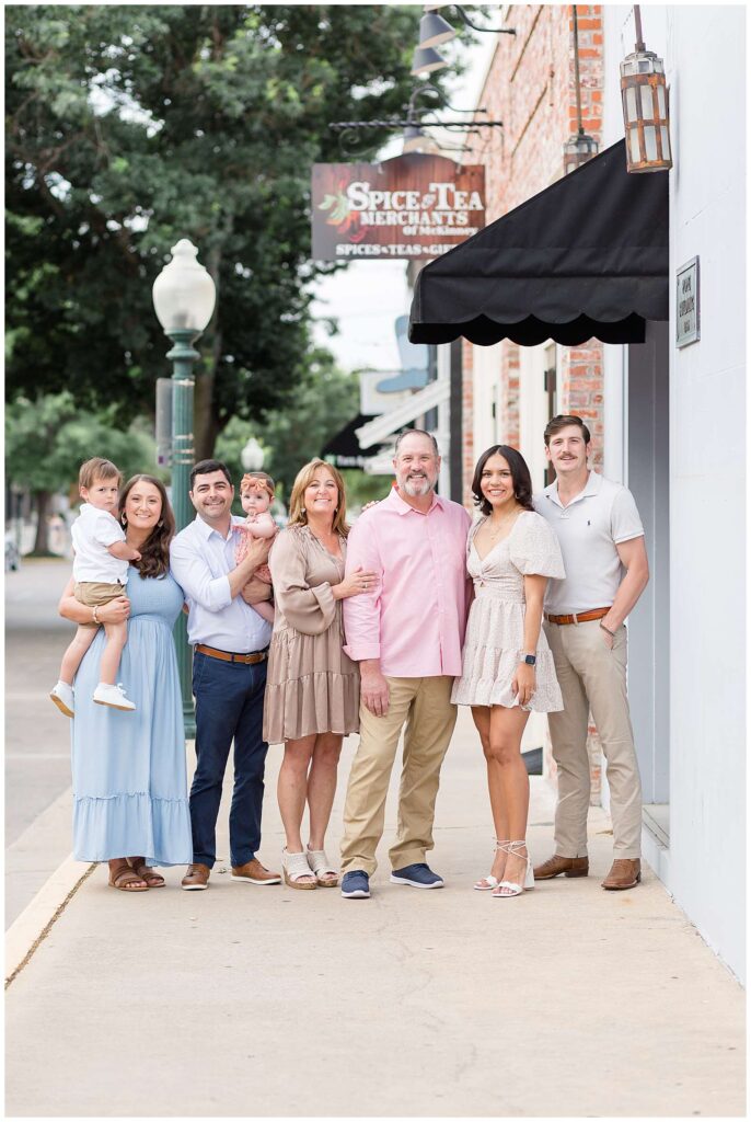 Extended family portraits with photographer, Wisp + Willow Photography Co., capture a special time with 6 adults and two young children.  They have their family session in McKinney, TX in Downtown Square.
