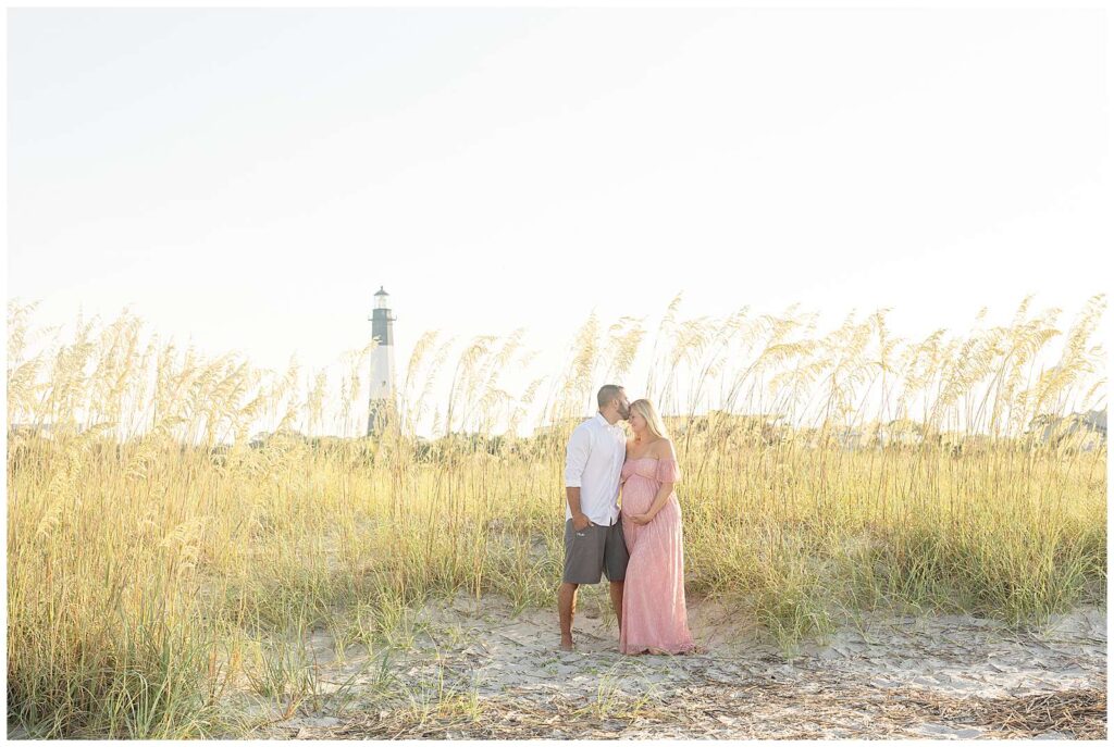 This Tybee Island Maternity Beach Session was a favorite!  Mom to be wore a lace, pink, off the shoulder dress showing off her baby bump and husband wore a white button up shirt and khakis.  They stand together on the beach surrounded with sea grass and the lighthouse behind them.