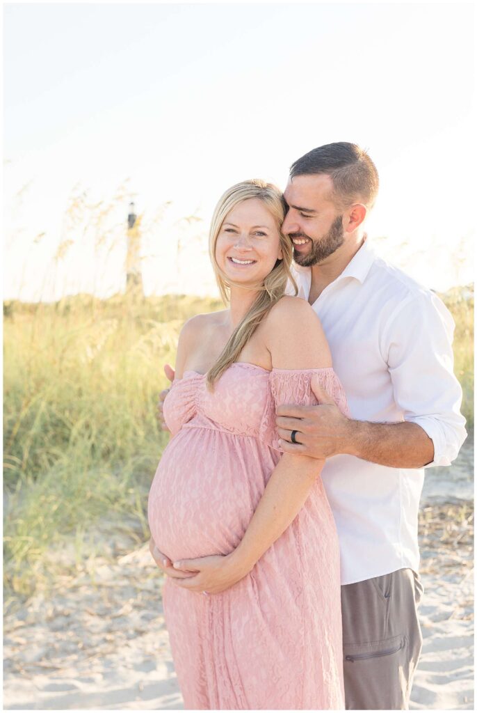 Wisp + Willow Photography Co. capture couple who is expecting their first child.  This maternity session showcases expecting parents at Tybee Island wearing a pregnant momma who is wearing a pink, lace dress and her husband wears a white button down shirt and grey shorts.