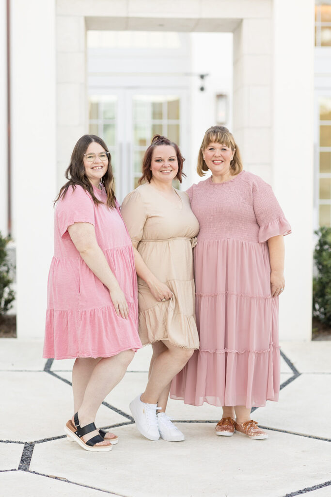 Texas family photographer, Wisp + Willow Photography Co, take branding photos of their admin team in Florida.  3 women stand together with the ends wearing light, pink dresses, and the one in the middle wears a neutral color dress.