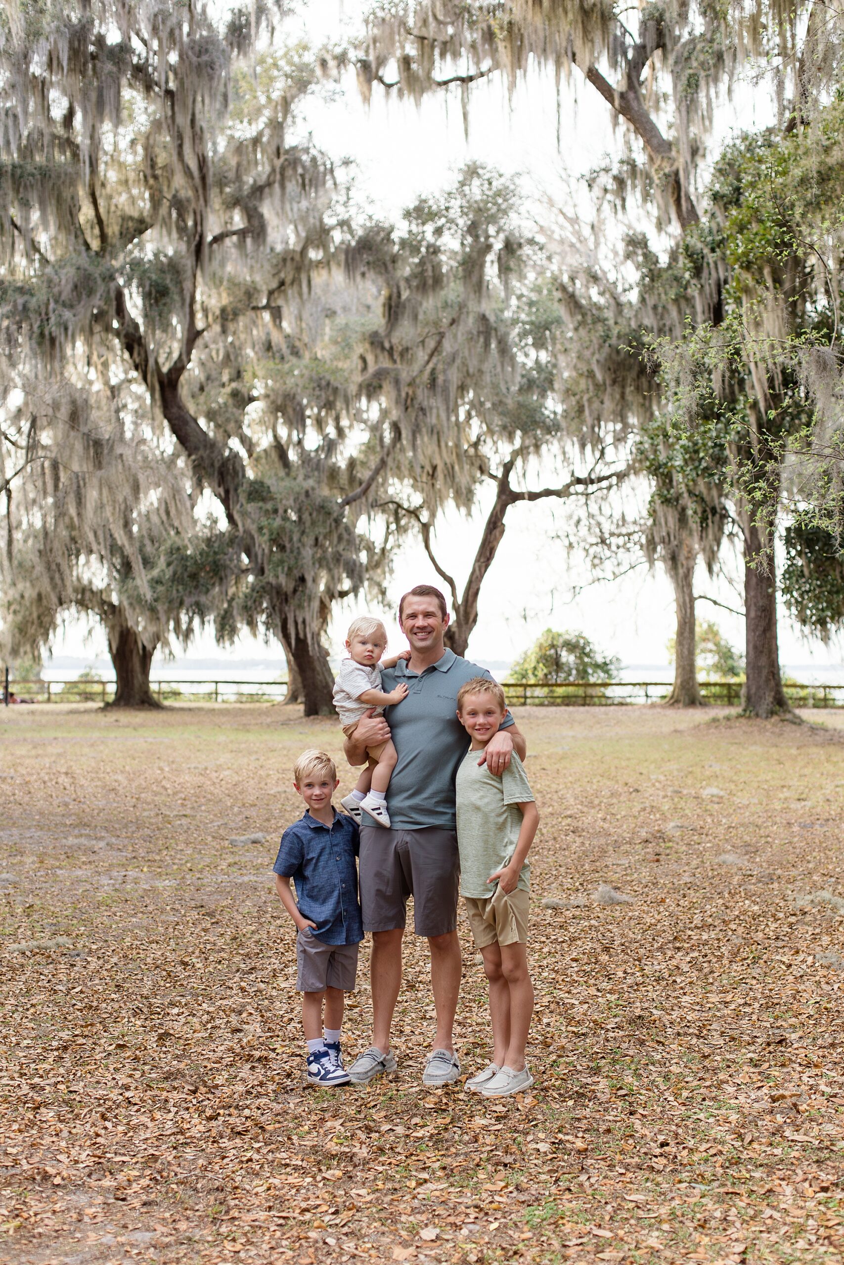 Dad poses with 3 sons under spanish moss trees at Alpine Groves Park for Jacksonville family session with Wisp + Willow Photography Co. 