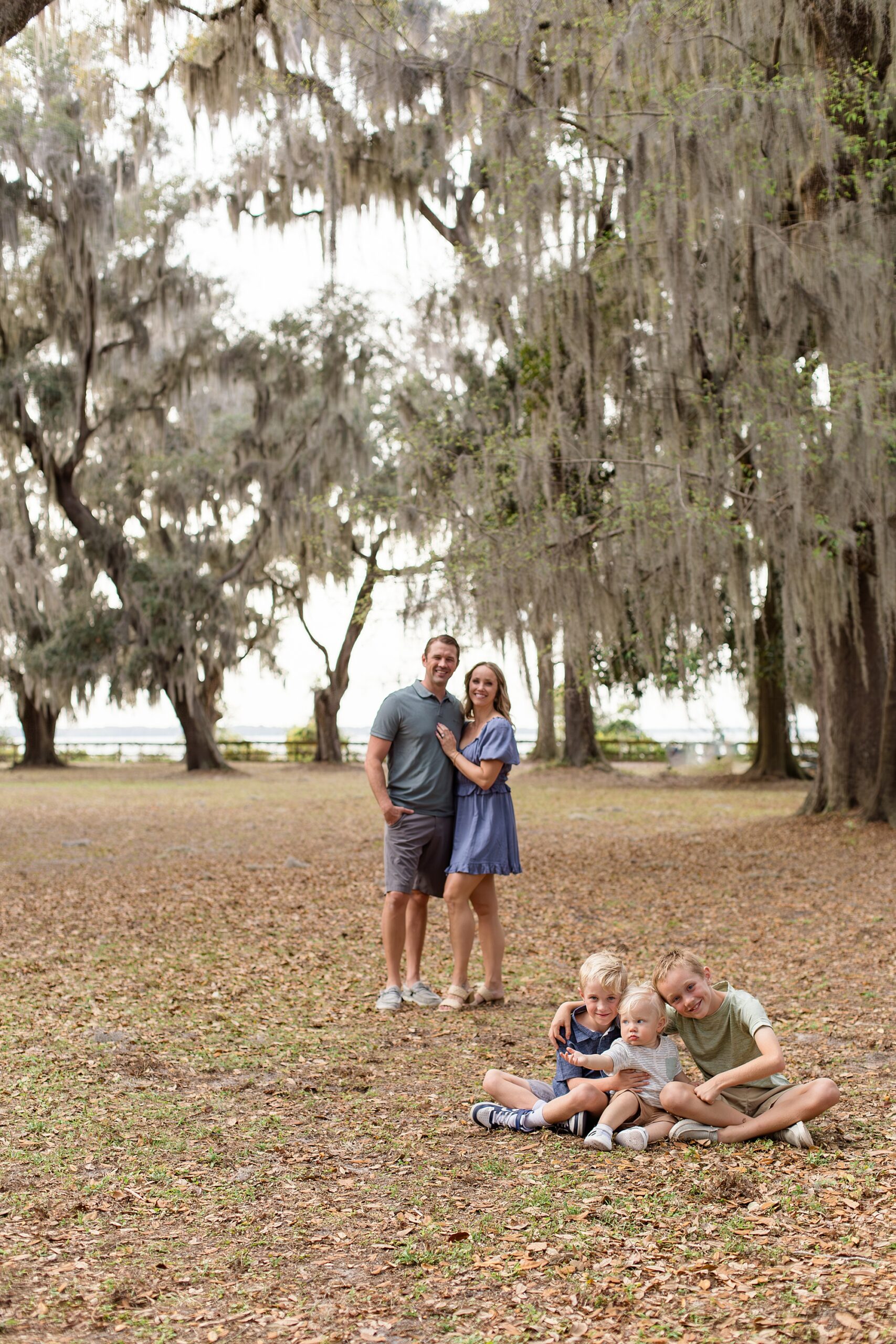 Parents pose in the background while kids sit in grass with Jacksonville Family Photographer, Wisp + Willow Photography Co. 