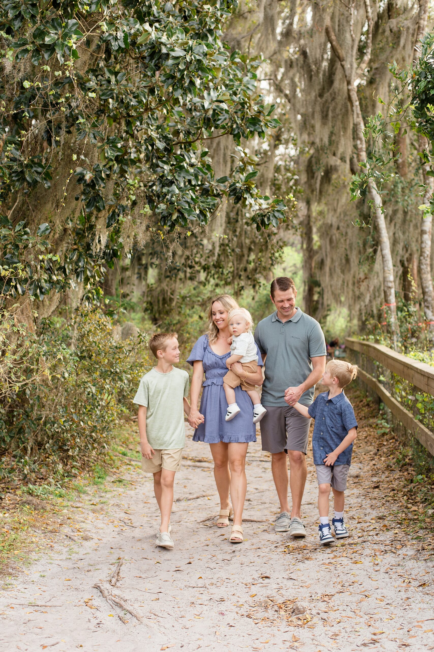 Family of 5 walks down trail holding hands during family session in Jacksonville, FL with photography team Wisp + Willow Photography Co.